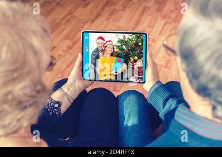 Senior couple celebrating Christmas chatting on digital tablet with son and daughter due to lockdown quarantine – Parents on videocall connecting with Stock Photo