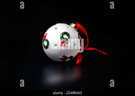 White bauble sphere with red ribbon decorated with Christmas wreath on black. New Year tree decoration Stock Photo
