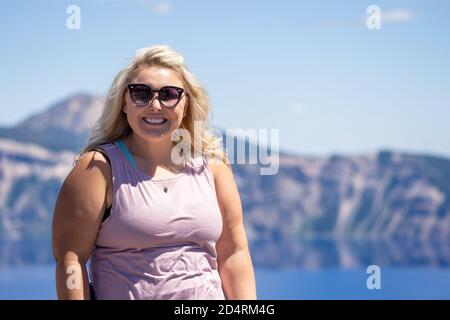 Stylish but casual blonde woman poses with sunglasses and a tank top at Crater Lake National Park Oregon Stock Photo