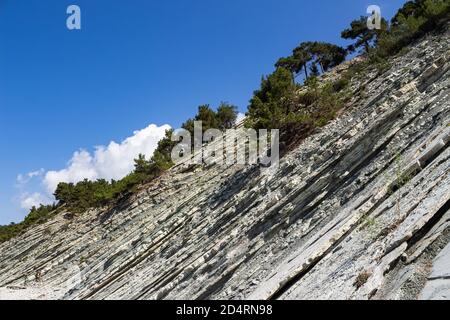 Picturesque rocks on a stone wild beach. A blue sky and a few clouds adorn the summer landscape. Forest and camping area Stock Photo