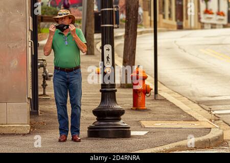 Ellicott City, MD, USA 10/07/2020: A middle aged caucasian man wearing Akubra hat, jeans and leather cowboy boots is putting on a face mask before cro Stock Photo