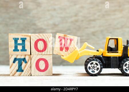 Toy bulldozer hold letter block w to complete word how to on wood background Stock Photo