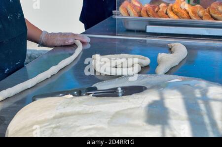 A baker rolls raw dough into a rope to make a hot, soft pretzel fresh from the oven Stock Photo