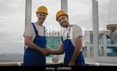 Handsome construction workers in protective helmets shaking hands. Stock Photo
