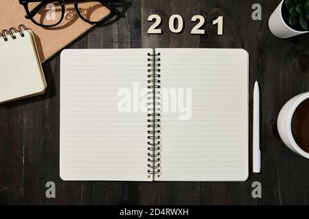 Yearly goals for 2021 - copybook, pen, cup of coffee, glasses and houseplant on wooden table Stock Photo