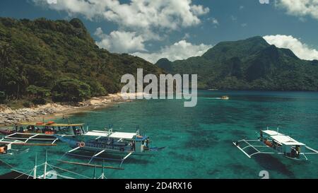 Ocean beach aerial: boat, people rest and swim at paradise resort. Amazing landscape of sand shore at sea bay water. Philippines tropical nature with jungle forest, mountains. Cinematic drone shot Stock Photo