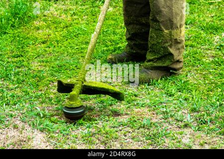 man in work clothes mows green grass with trimmer Stock Photo