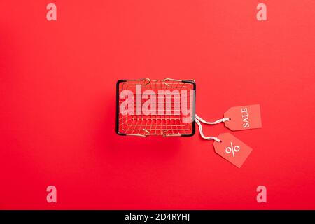 Black Friday sale concept. Empty shopping basket with sales tags on red background. Flat lay, top view. Stock Photo