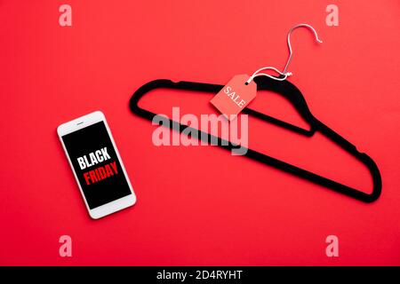 Black Friday concept. Mobile phone with sign 'Black Friday' on screen and hanger with label on red background. Flat lay, top view. Stock Photo