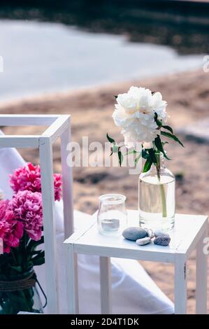 Close up details of wedding or holiday decor with peonies in a glass jar by the sea. Stock Photo