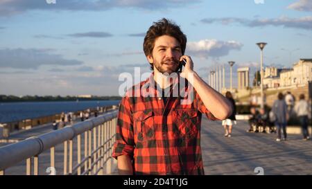 Handsome male student walking outdoors and talking on mobile phone. Stock Photo