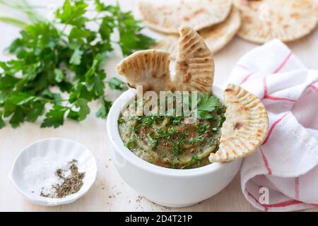 Eggplant dip in a white ceramic bowl with parsley and whole grain flat bread on a light wooden background Stock Photo