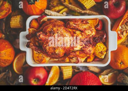 Festive turkey or chicken baked by Thanksgiving on white owen plate and a harvest of seasonal vegetables. Pumpkin, corn, apples, oranges and potatoes. Stock Photo