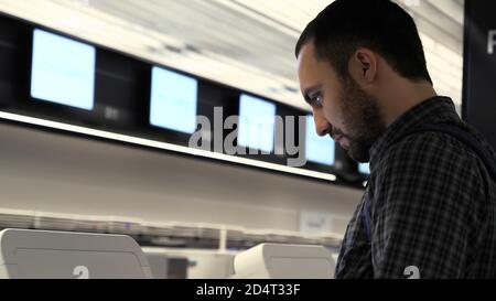 Young man with backpack touching interactive display using self service machine. Stock Photo
