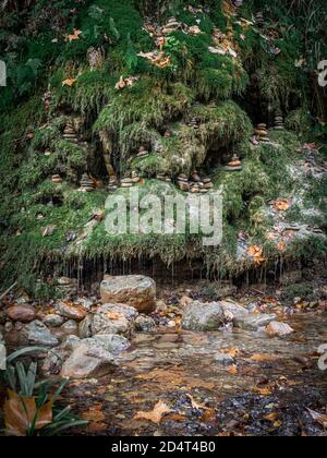 Fabulous autumn forest landscape of autumn forest with moss-covered waterfall with many cairns on it. Stones in the forest stream with autumn fallen l Stock Photo
