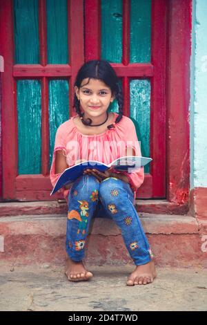 Teenager Village girl of Indian ethnicity seating at corridor and reading a book. Stock Photo