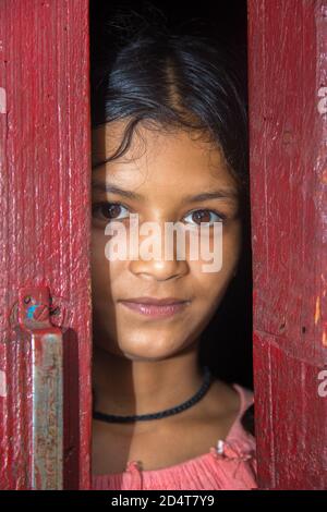 Asian, Indian beautiful teenager contemplating and standing by the door while looking at camera with smiling on her face Stock Photo