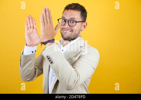 Young handsome businessman wearing suit over isolated yellow background clapping and applauding happy and joyful, smiling proud hands together Stock Photo