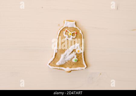 Bell-shaped gingerbread cookies, decorated with glaze and multi-colored sprinkles, on white painted wood texture. Stock Photo