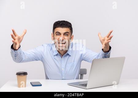 Irritated man boss sitting office workplace, stretching hands to camera, looking furious while shouting with anger, evil crazy grimace, conflict at wo Stock Photo