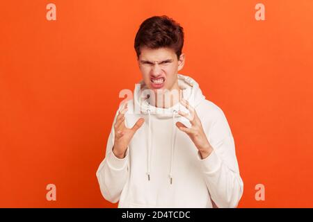 Extremely angry frustrated teenager in casual style sweatshirt with hood dissatisfied with service, scary grin on his face. Indoor studio shot isolate Stock Photo