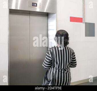 Back view of woman waiting for elevator inside a building Stock Photo
