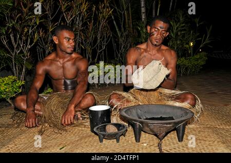 Two Fijians squat on matting at a tourist show to serve Fiji's national drink, Yaqona, also called Kava in Fiji in the South Pacific.   Yaqona or Kava Stock Photo