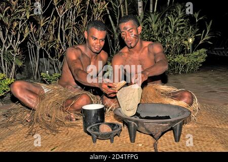 Two Fijians squat on matting at a tourist show to serve Fiji's national drink, Yaqona, also called Kava in Fiji in the South Pacific.   Yaqona or Kava Stock Photo