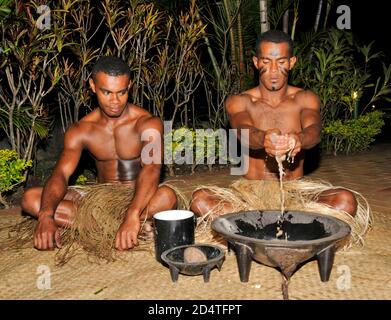 Two Fijians squat on matting at a tourist show to serve Fiji's national drink, Yaqona, also called Kava in Fiji in the South Pacific.   Yaqona or Kava Stock Photo