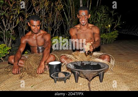 Two Fijians squat on matting at a tourist show to serve Fiji's national drink, Yaqona, also called Kava in Fiji in the South Pacific.   Yaqona or Kava Stock Photo