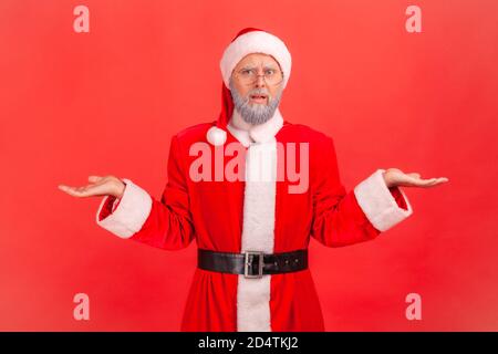 Disappointed portrait of confused gray bearded elderly man in eye glasses and santa claus costume throws up hands, cant understand how to spend holida Stock Photo