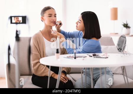 Asian Woman Doing Makeup For Her Beautiful Model Stock Photo