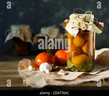 Homemade jars of pickled tomatoes on a rustic wooden background. Pickled and canned product. Fermented tomatoes on a dark background. Stock Photo