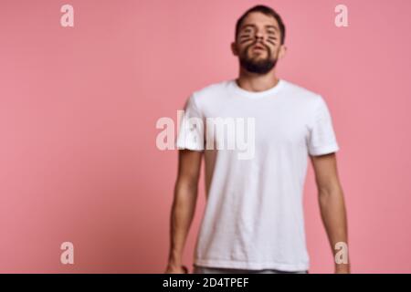 Emotional man with a baseball bat in his hand on a pink background and black lines on the face of the model grimace Stock Photo