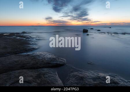 Twilight sunset over rocky shore of Baltic sea. Almost clear sky and orange strap along the horison. Estonia. Stock Photo