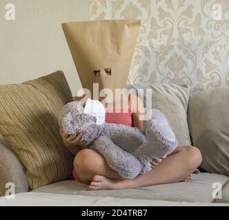 Stay at home quarantine coronavirus prevention of the pandemic. A sad child and his Teddy bear both in protective medical masks are sitting on the sofa. Prevention of the epidemic Stock Photo