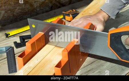 Man cutting a slat of wood using a saw and miter box. Close up view. Selective focus. Stock Photo
