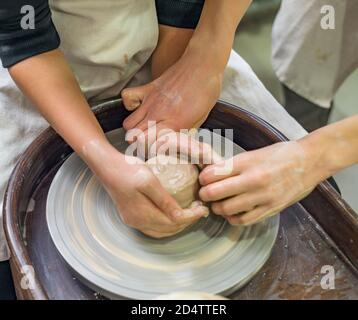 A potters hands guiding a child hands to help him to work with the ceramic wheel and clay. Close up photo from workshop. Learning in progress. Stock Photo