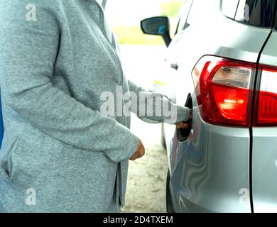 A woman's hand in a gray jacket opens the gas tank of a silver car at a gas station. Close-up view. Stock Photo