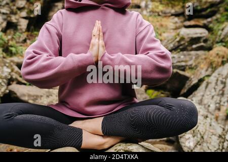 Crop of a young woman sitting on big stone cross-legged with joined hands Stock Photo