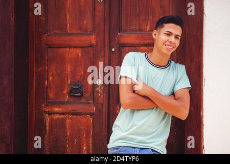 Young Hispanic man smiling with crossed hands against the door and white wall Stock Photo