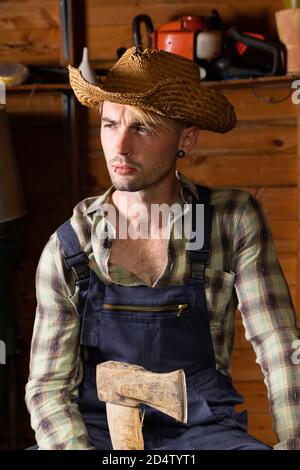 Young man in his 20s wearing dungarees and holding an axe. Stock Photo