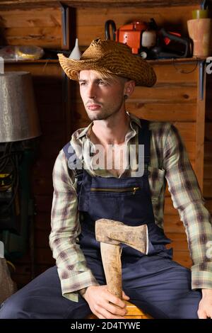 Young man in his 20s wearing dungarees and holding an axe. Stock Photo