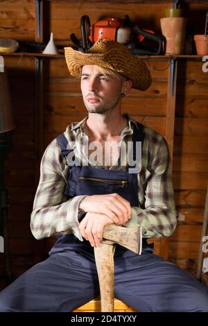 Young man in his 20s wearing dungarees and holding an axe. Stock Photo