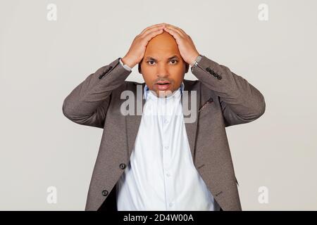 Surprised young male African American businessman holding his hands behind his head, absolutely shocked by the news. standing on a gray background. Human face expression concept Stock Photo