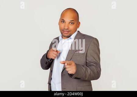 Young male African American businessman pointing at camera with index fingers on both hands with happy facial expression. Copy space. Isolated on gray background, advertising concept Stock Photo