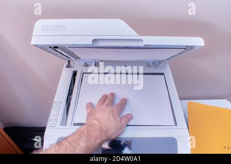 A white or Caucasian man is working in the office making photocopies on a white copier with the top cover open Stock Photo
