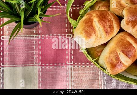 Delicious freshly baked and browned milk bread buns in a wicker basket on a red and white checkered tablecloth Stock Photo