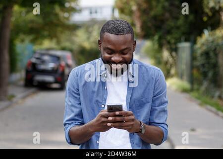 Handsome Afro-American man using smartphone and smiling. Happy man using mobile phone apps, texting message, browsing internet, looking at smartphone Stock Photo
