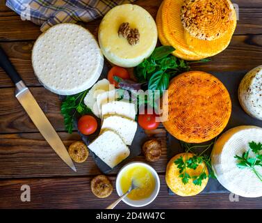 Cheese Heads with cheeses of different kinds. Assortment of different cheese types on wooden background. Fresh dairy product, various greens, nuts, honey, healthy organic food. Delicious apetizer. Countryside market. Home-made cheese. Flat lay, top view. Stock Photo